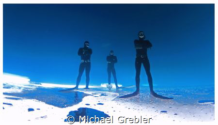Three free-divers strike a pose upside down under the ice... by Michael Grebler 